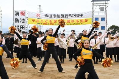 吹奏楽部が演奏している前でポンポンを持ってダンスをしている女子学生の写真
