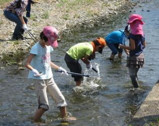 子供達4人が川に入ってゴミ拾いをしている写真